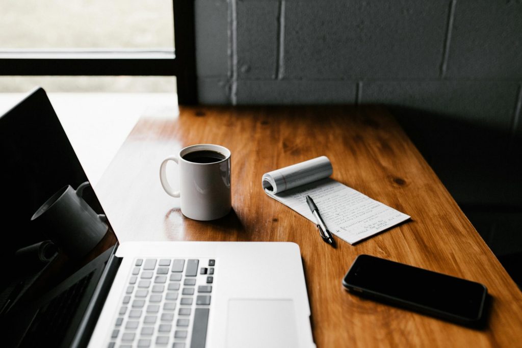 Un espace de travail bien rangé comprenant un ordinateur portable, une tasse à café, un téléphone et un bloc-notes sur un bureau en bois.