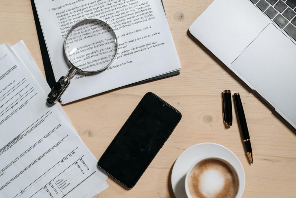 Vue de dessus des documents, de l'ordinateur portable, du café et de la loupe sur le bureau.